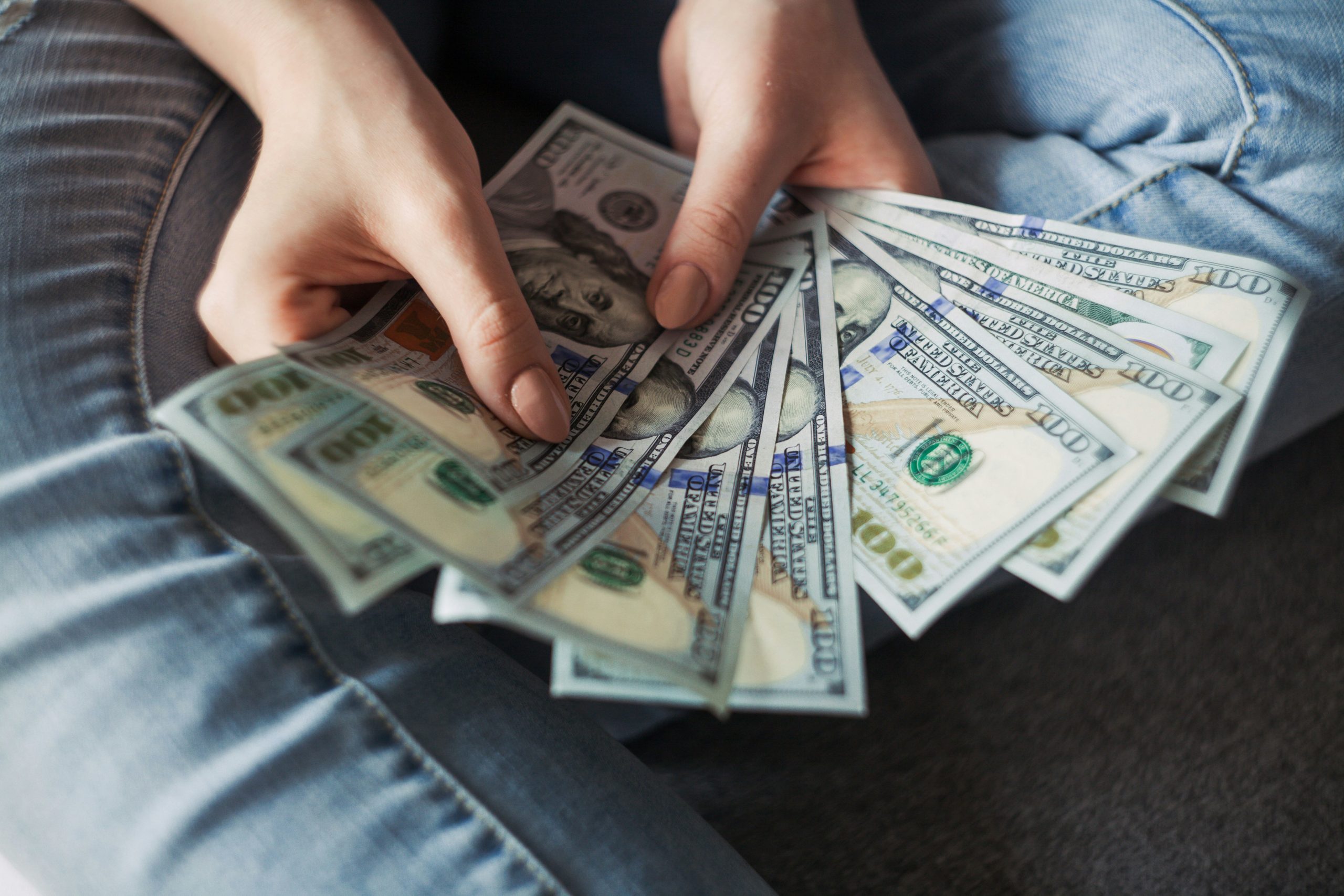 A person's hands holding multiple hundred dollar bills